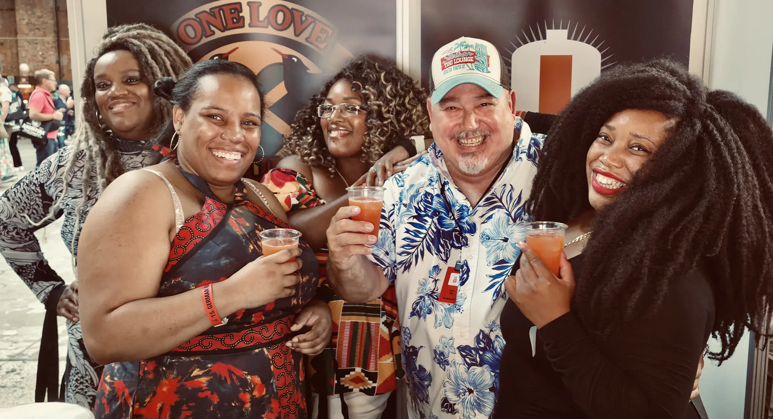 Raising cups of rum punch with fans at the Warehouse #1 stand, in front of the One Love Rum Punch and Warehouse #1 banners